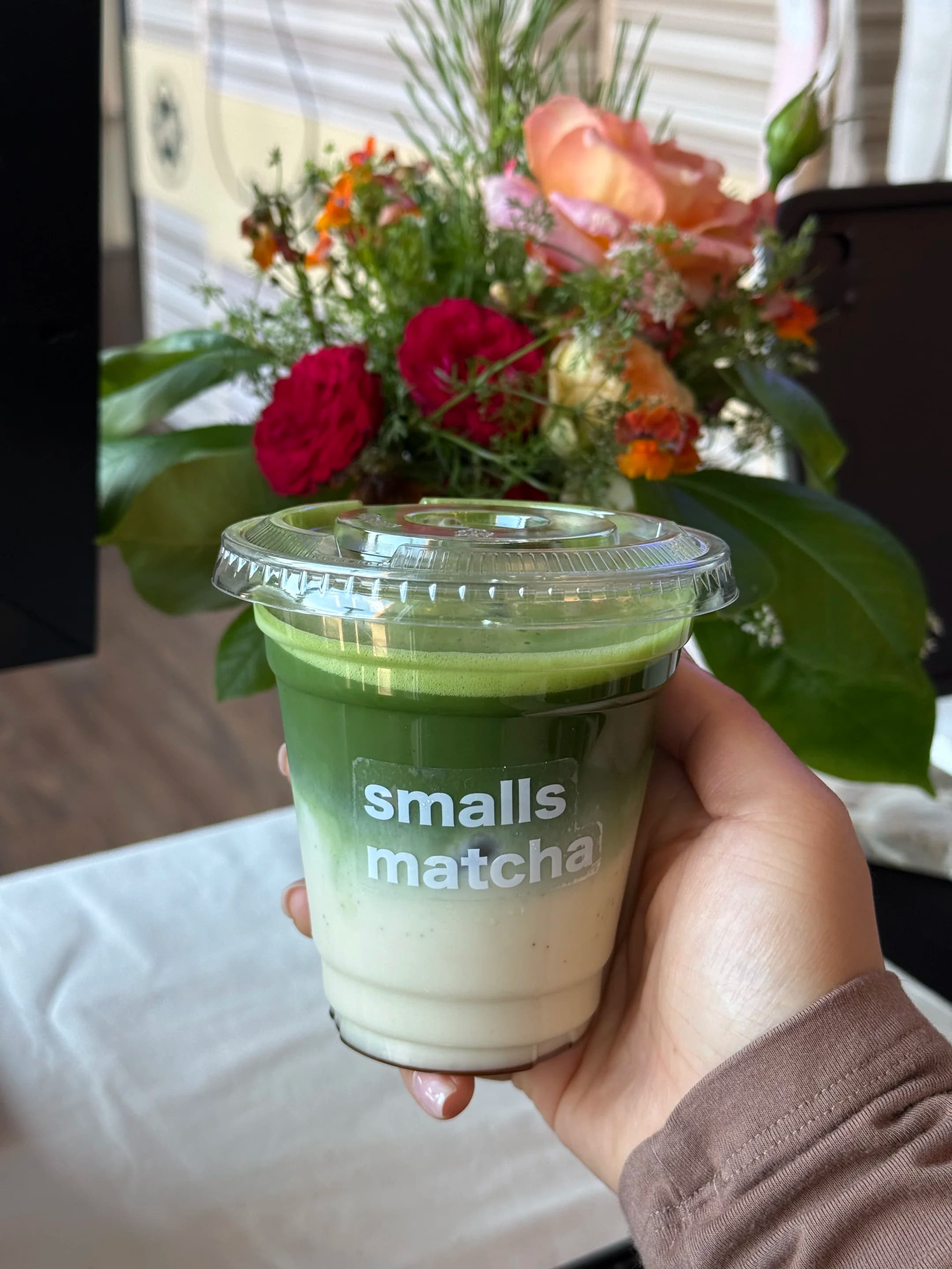 a smalls matcha drink in a branded cup, held in front of a floral arrangement